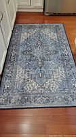 Full view of the blue patterned kitchen rug laid on hardwood floor near kitchen cabinets and fridge.