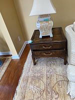 Full view of wooden side table next to sofa with lamp on top, showing the table's square shape and the drawer handles.