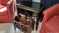 Shows the black lacquered side table with golden accents and the wooden magazine rack positioned beneath it, highlighting the overall look and placement.