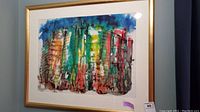 Frontal view of the framed watercolor painting showing the colorful abstract cityscape in a gold frame.