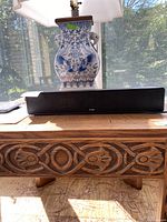 ZVOX AV157 sound bar on a wooden carved furniture piece with a decorative blue and white vase behind it.