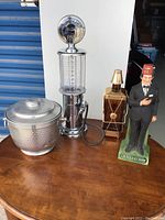 Overall view of the four items placed on a wooden table against a white and blue background showing the ice bucket, liquor dispenser, music bottle and novelty figurine