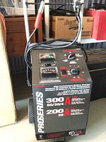 Front view of battery charger unit with cables draped over handle, showing ProSeries branding and amperage ratings.