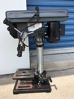 Side-front view of the whole drill press showing base, column, adjustable table, motor, and operating handles.