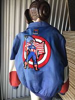 Back view of Captain America leather jacket showing Captain America figure with American flag patch and shield target background, blue leather with red and white sleeves.