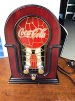 Front view of Coca-Cola AM/FM radio designed to look like a vintage jukebox with Coca-Cola logo and bottle graphic on front.