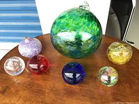 Photo showing all seven glass globes arranged on a wooden surface highlighting sizes, colors, and textures.