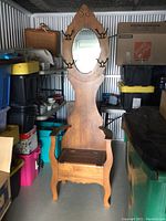 Full view of wooden hall storage bench with attached oval mirror and several black metal coat hooks on sides.