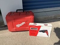 Milwaukee red plastic carrying case with white logo next to Jobmate 3.5 amp hand drill box outside.
