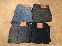 Four pairs of Levi Strauss & Co. jeans in folded arrangement showing back pockets, varying shades of blue denim, each with leather patch and red tab.