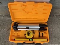 Full view of the opened orange carrying case containing the tripod, rotary laser level, leveling rod, and small mounting accessories.