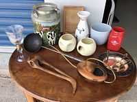 Full lot of assorted decorative and kitchen items including painted milk can, glassware, vases, copper tray, ladle, wooden tongs, and Coca-Cola jar on wooden surface.
