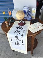 Wide angle photo showing all decor items arranged on a wooden table including globe, blue and white vases, hourglass, glass flowers, scroll, paper bundles and decorative box.