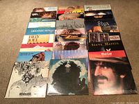 Overview shot of 16 vinyl record sleeves arranged on carpet.