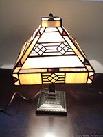 Front view of the stained glass pyramid-shaped table lamp illuminated on a surface