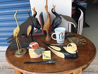 Overview of bird-themed items on a wooden table including metal and wooden figurines, plush bird, mug, and trivet
