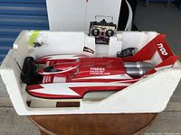 Full view of red and white Tyco Unlimited Hydroplane R/C boat in white foam packaging with included remote control and charger.