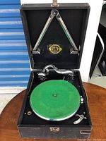Overview of phonograph inside black carrying case, showing green felt turntable mat and chrome tonearm with sound horn.