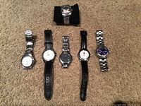 Full view of six watches laid on carpet showing a mix of leather and metal bands, various dial colors and styles