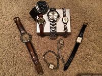 Overview of seven used watches laid out on carpet showing variety of styles and conditions.