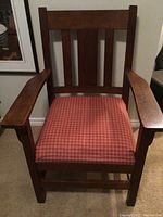 Wooden armchair seen from front, showing cushioned red checkered seat, wooden armrests, and slat backrest with minor signs of wear.