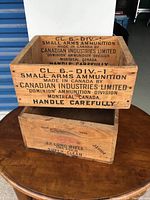 Two wooden crates stacked on a round wooden table showing exterior stenciled text.