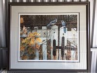 Full view of framed art print depicting two blue jays on a white picket fence surrounded by autumn leaves and branches.