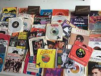 Collection of multiple 45 RPM vinyl singles showing various record sleeves and vinyl labels from multiple artists and labels