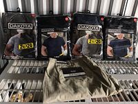 Four sealed packages of Dakota men's work T-shirts displayed on a metal shelf. Two packages show black T-shirts, two show navy T-shirts, all labeled size 2XL/2TG.