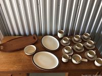 Full view of ceramic dishware including platters, cups, saucers, creamer, sugar bowl, and wooden tray on wooden table