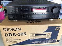 Denon DRA-395 stereo receiver on top of its original box showing front panel with display, buttons, and volume knob.