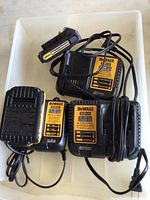 Overview of four DeWalt items including two battery chargers and two battery packs inside a plastic bin.
