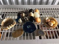 Wide shot showing a collection of polished stone eggs, geode slices, and various crystals arranged on a white surface.