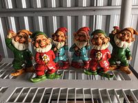 Front view of all seven gnome elf figurines lined up on a shelf showing varied poses and colorful outfits.
