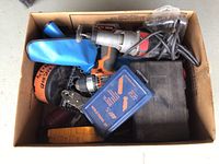 Top view of cardboard box containing assorted tools including a drill, drill bit cases, and bolt cutter handles