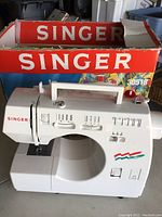 White Singer sewing machine with original box showing the brand name and model number.