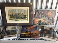 Shows two framed vintage train prints and three railroading books arranged on a shelf or bench.