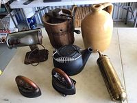 Top-down view of all items arranged on table showing full assortment including churn, jug, two irons, teapot, fire extinguisher, and heater fan