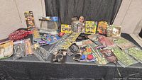 Wide view of all costume accessories spread out on a dark cloth background including wigs, glasses, makeup palettes, jewelry, Halloween props, and a nurse stethoscope.
