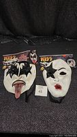 Two Kiss band masks - The Demon with tongue out and The Star Child with a black star over the eye, both placed side by side showing signs of discoloration and age.