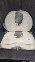 Two pairs of large white feathered angel wings stacked, packaged in clear plastic wrap.