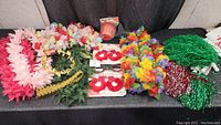 Wide view of assorted costume accessories on a table including leis, pom-poms, novelty glasses, and a headband.