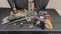 Full view of all costume accessories laid on black table, including swords, pirate hook, gold toy gun, and necklaces.