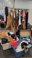 Wide view of costumes hanging on a rack and bins of assorted costume accessories on the floor.