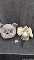Photo showing both the grey bulldog and grey elephant mascot heads side by side on black fabric background.