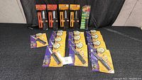 Full lot arranged on table showing 10 sealed retractable prop knives in packaging and one multi-pack of glow sticks.