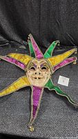 Full view of the jester mask showing colorful fabric points in gold, purple, and green with silver trim and bells at the tips.