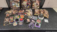 Wide view showing multiple theatrical makeup palettes, fake mustaches, scar and wound kits, cream makeup jar, and face paint palettes arranged on a black surface.