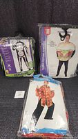 Three men's costumes in sealed packaging, including skeleton, hamburger sandwich, and Hawaiian shirt designs.