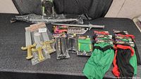 Top-down photo of all items spread out showing toy swords, plastic sai, and various ninja costume accessories in black and green, including gloves and arm bands.
